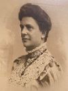 Clara A. Fuller: Sepia-toned portrait of a woman with an updo hairstyle, wearing a high-necked, lace-trimmed Victorian-style dress, facing left.