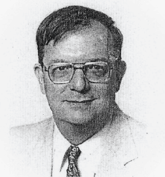 Larry C. Spongberg: A middle-aged man with short dark hair wearing glasses, a light-colored suit, a white shirt, and a patterned tie, facing the camera with a neutral expression.